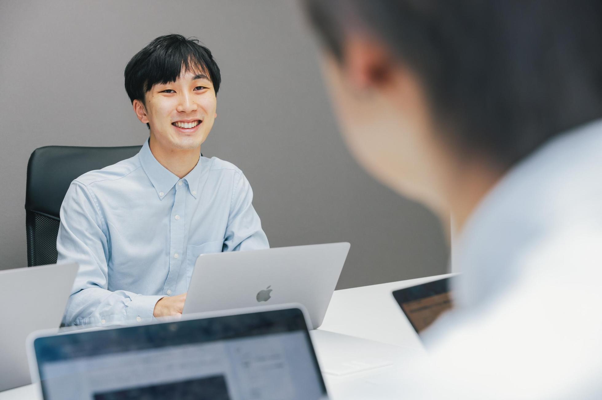 会議室でノートPCを開き、笑顔で面談に応じる水色シャツの若手エンジニア
