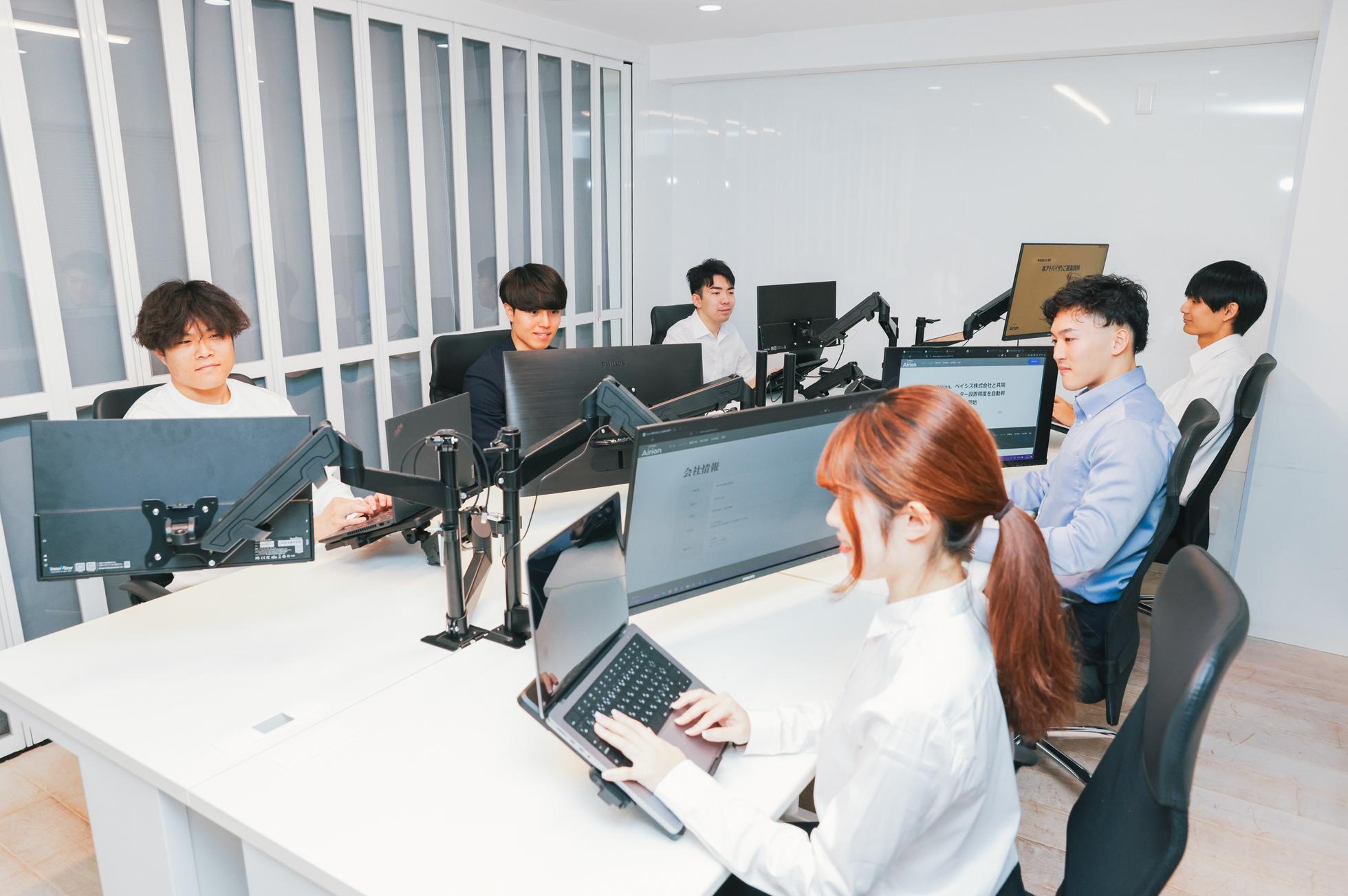 Team members working at monitor-equipped desks in a bright white office