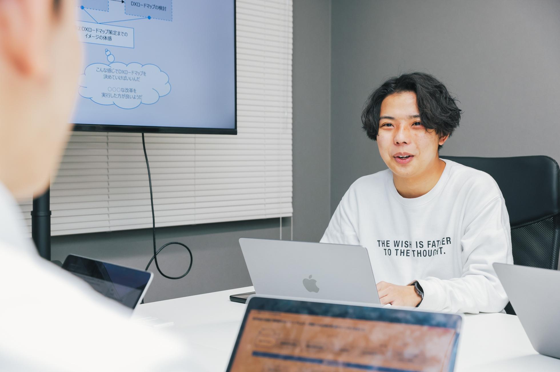 An engineer working on a laptop in a meeting room, with a DX roadmap slide shown on the display