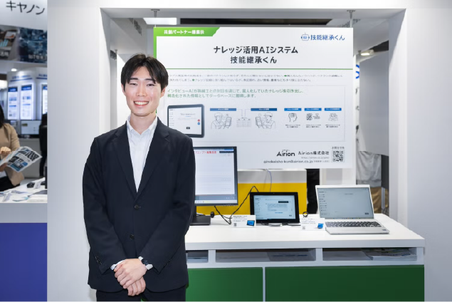EdgeTech+ 2025の共同出展ブースで「技能継承くん」のパネルとデモ端末の前に立つAirion社員