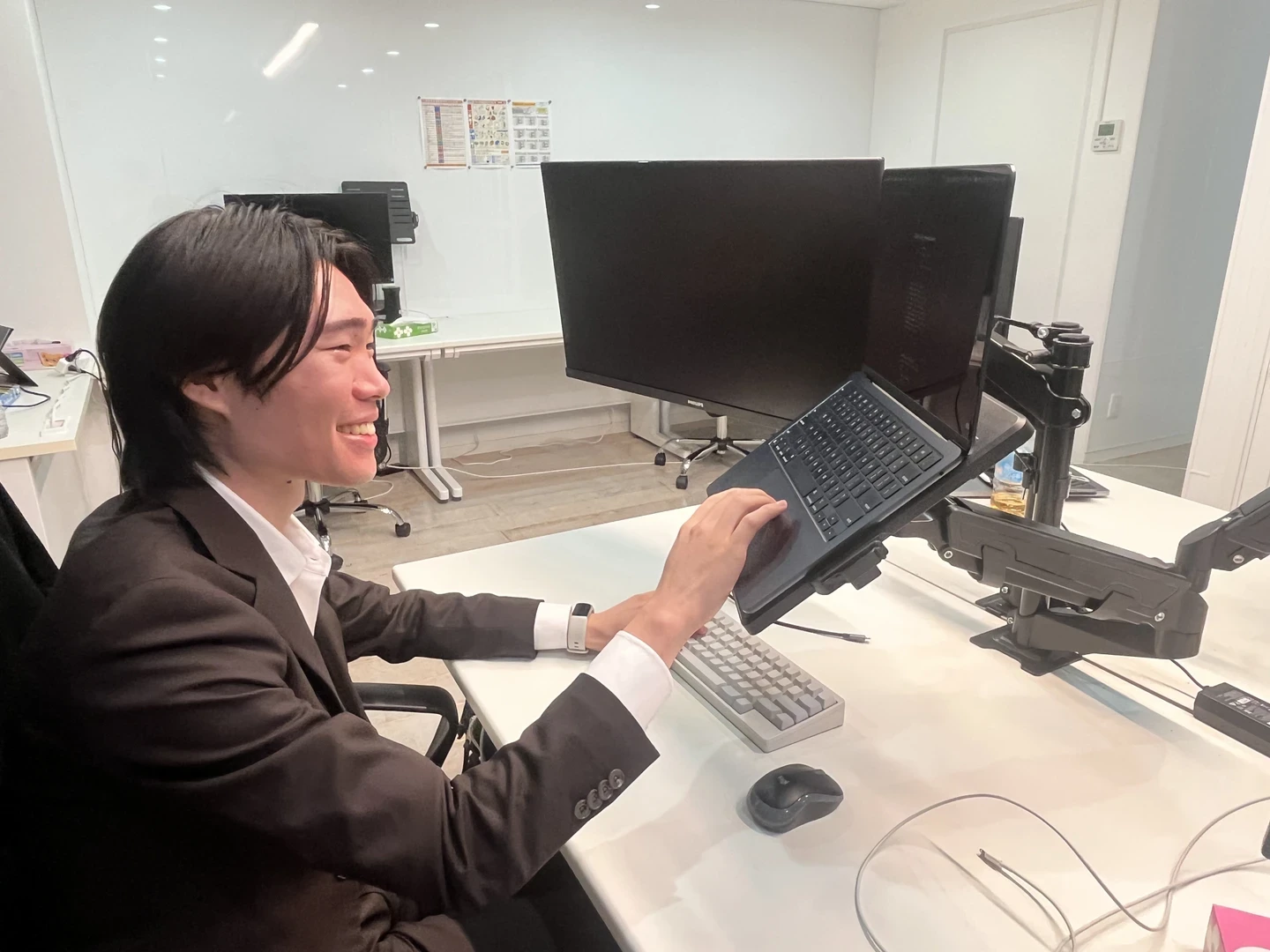 モニターアームに設置したノートPCを操作しながら笑顔で話す小安